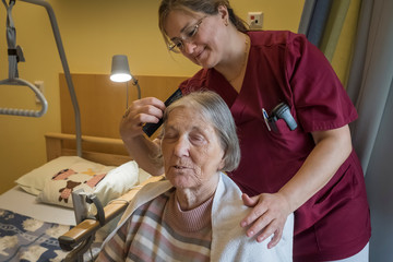 Eine Fachpflegerin in weinroter Funktionskleidung kämmt das Haar einer Hospizgästin an deren Pflegebett in einem Gästezimmer des Diakonie Hospiz Volksdorf in Hamburg-Volksdorf. Eine Fachpflegerin in weinroter Funktionskleidung kämmt das Haar einer Hospizgästin an deren Pflegebett in einem Gästezimmer des Diakonie Hospiz Volksdorf in Hamburg-Volksdorf.
