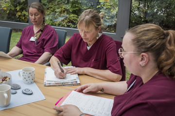 Drei Fachpflegerinnen in weinroter Funktionskleidung sitzen auf der Terrasse an einem Tisch mit Dokumenten bei einer Besprechung im Diakonie Hospiz Volksdorf in Hamburg-Volksdorf. Drei Fachpflegerinnen in weinroter Funktionskleidung sitzen auf der Terrasse an einem Tisch mit Dokumenten bei einer Besprechung im Diakonie Hospiz Volksdorf in Hamburg-Volksdorf.