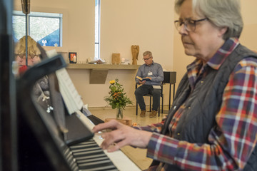 Eine ehrenamtliche Helferin spielt an einem Klavier in Begleitung von Seelsorger Roger Bahr in einem festlich geschmückten Raum mit einem Fenster in Kreuzform im Diakonie Hospiz Volksdorf in Hamburg-Volksdorf. Eine ehrenamtliche Helferin spielt an einem Klavier in Begleitung von Seelsorger Roger Bahr in einem festlich geschmückten Raum mit einem Fenster in Kreuzform im Diakonie Hospiz Volksdorf in Hamburg-Volksdorf.