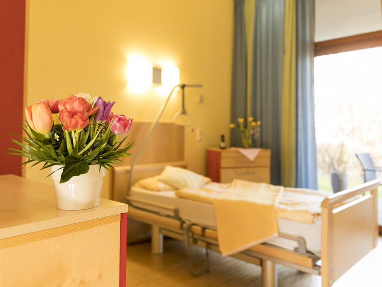 Blick in ein helles Gästezimmer mit Bett und Blumenstrauß, Hospizangebot in Hamburg und Umgebung, Diakonie Hospiz Volksdorf Blick in ein helles Gästezimmer mit Bett und Blumenstrauß im Diakonie Hospiz Volksdorf